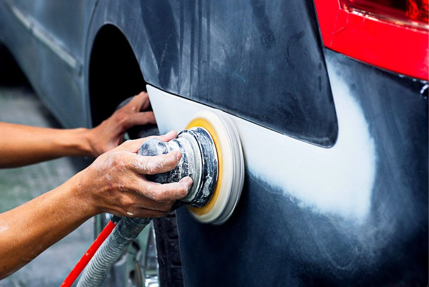 Person polishing a black car with a power buffer in a garage.