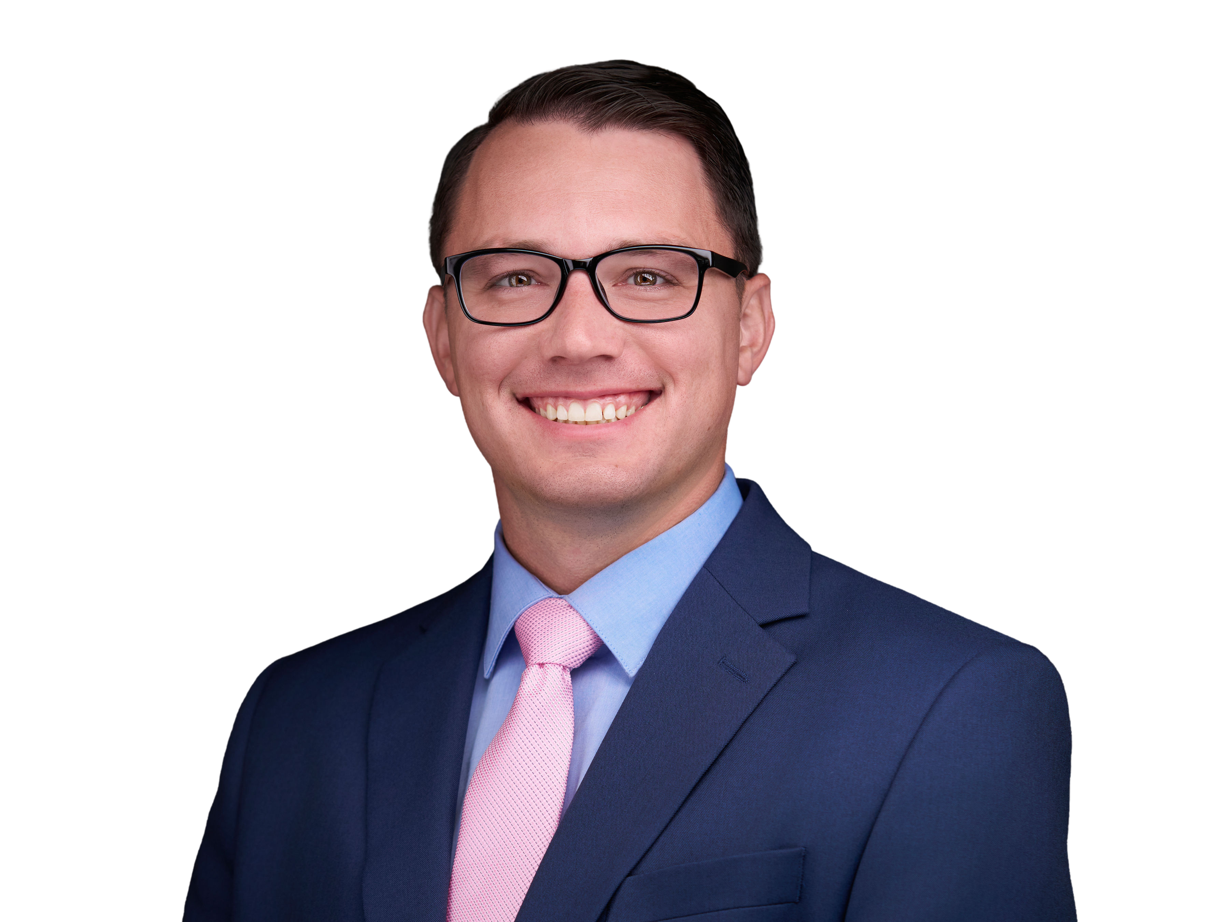A young man with glasses, wearing a blue suit, a light blue shirt, and a pink tie, smiling against a plain background.
