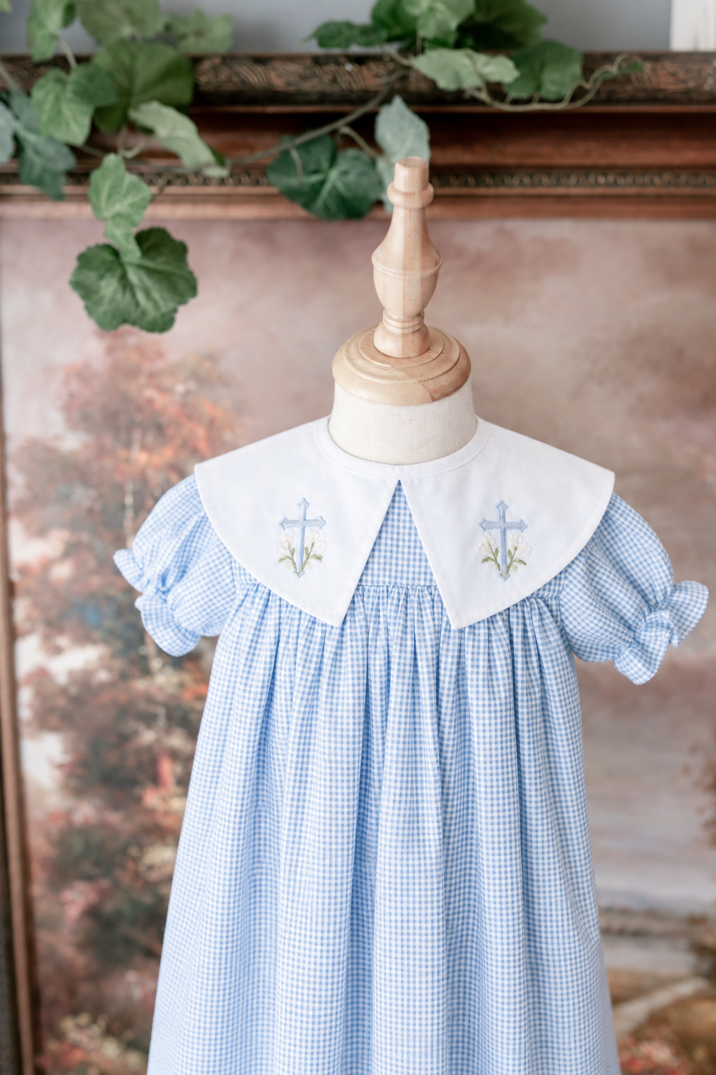 Childs dress with a white collar embroidered with crosses and floral symbols, featuring a blue and white checkered pattern, displayed on a dress form.