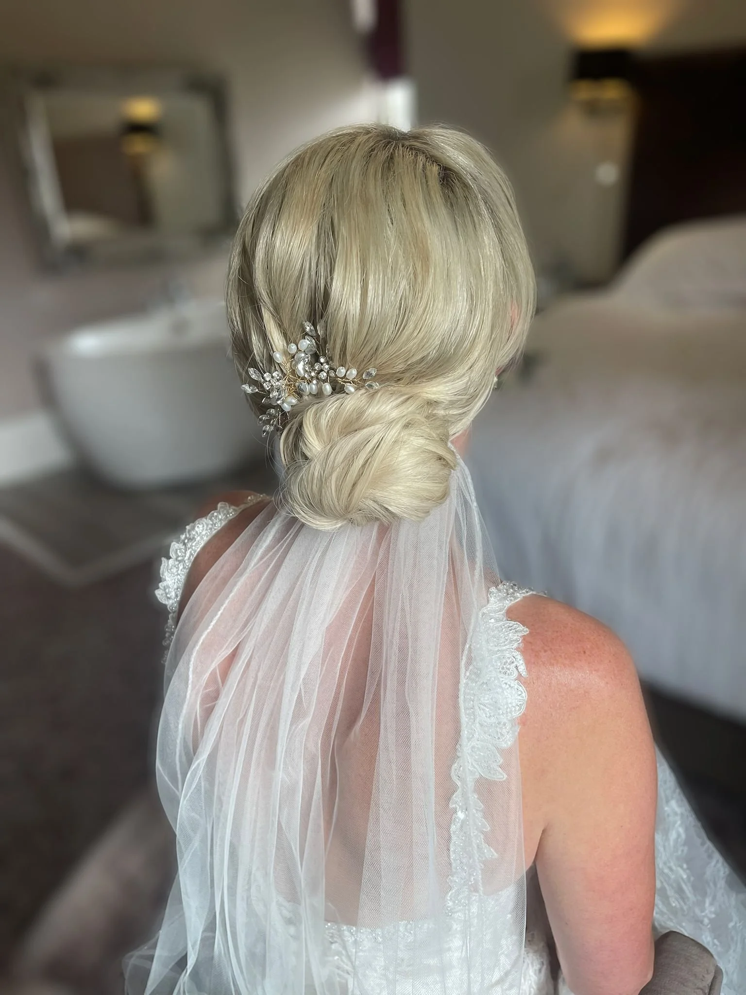 Low bridal bun with veil placed underneath finished off with beautiful bridal hairpiece