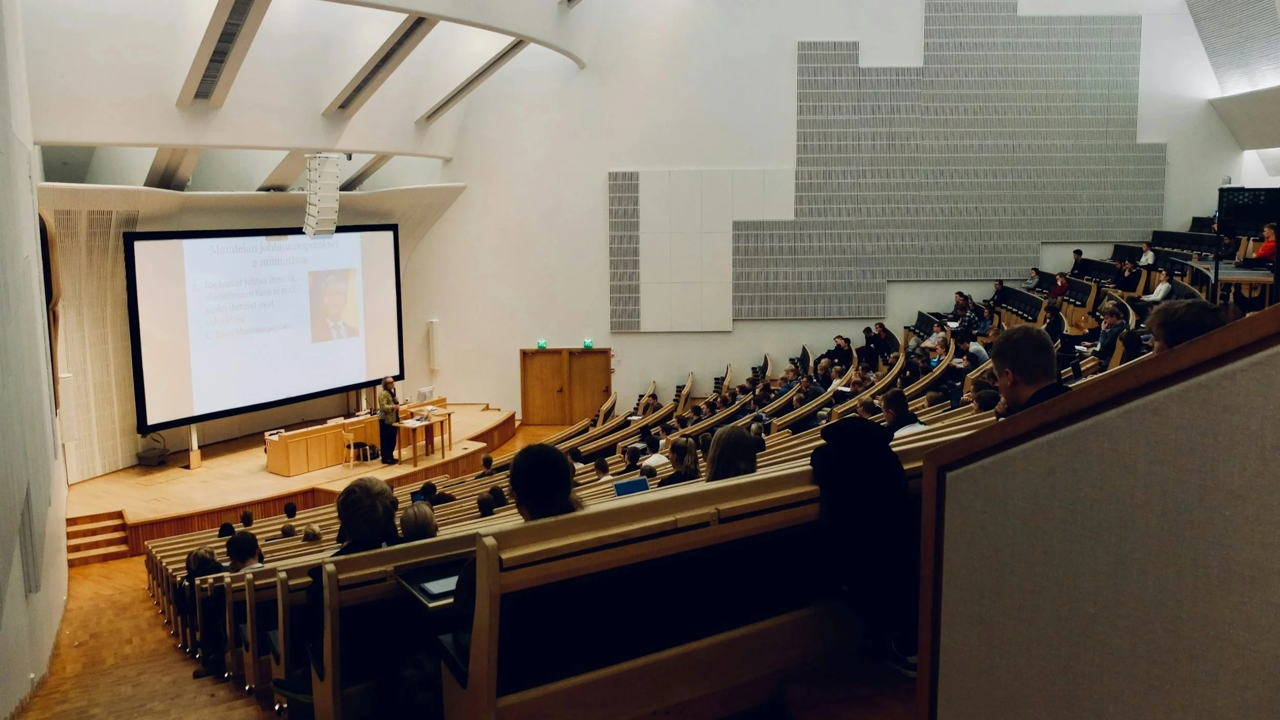 A college lecture hall with professor at the front of the class and students in their seats.