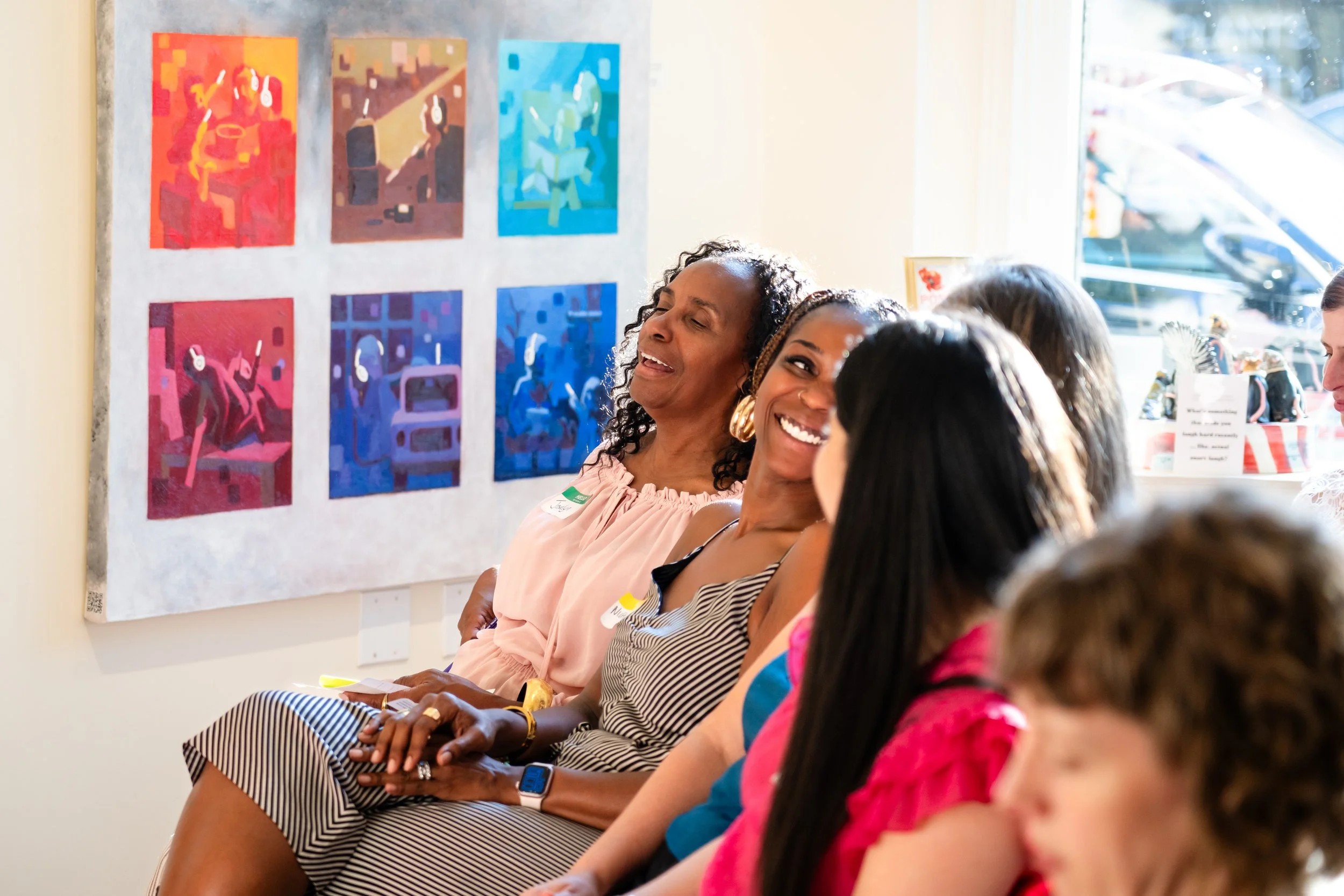 Three women sharing a laugh with an art installation in the background.