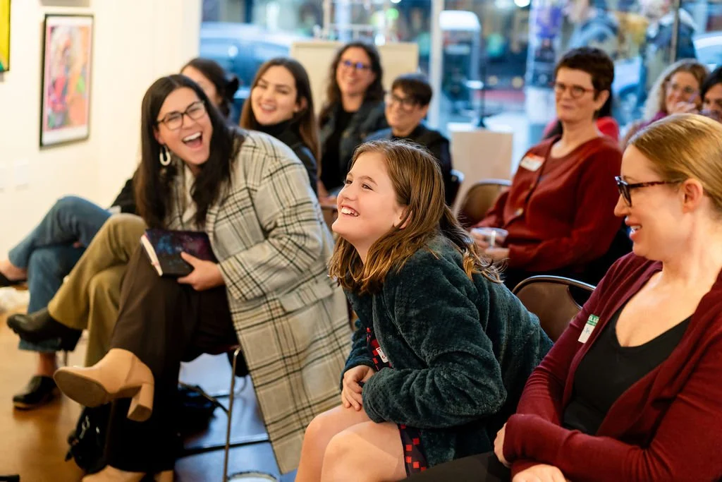 Rows of women, with two leaning forward and laughing, while others look on with shared laughter.