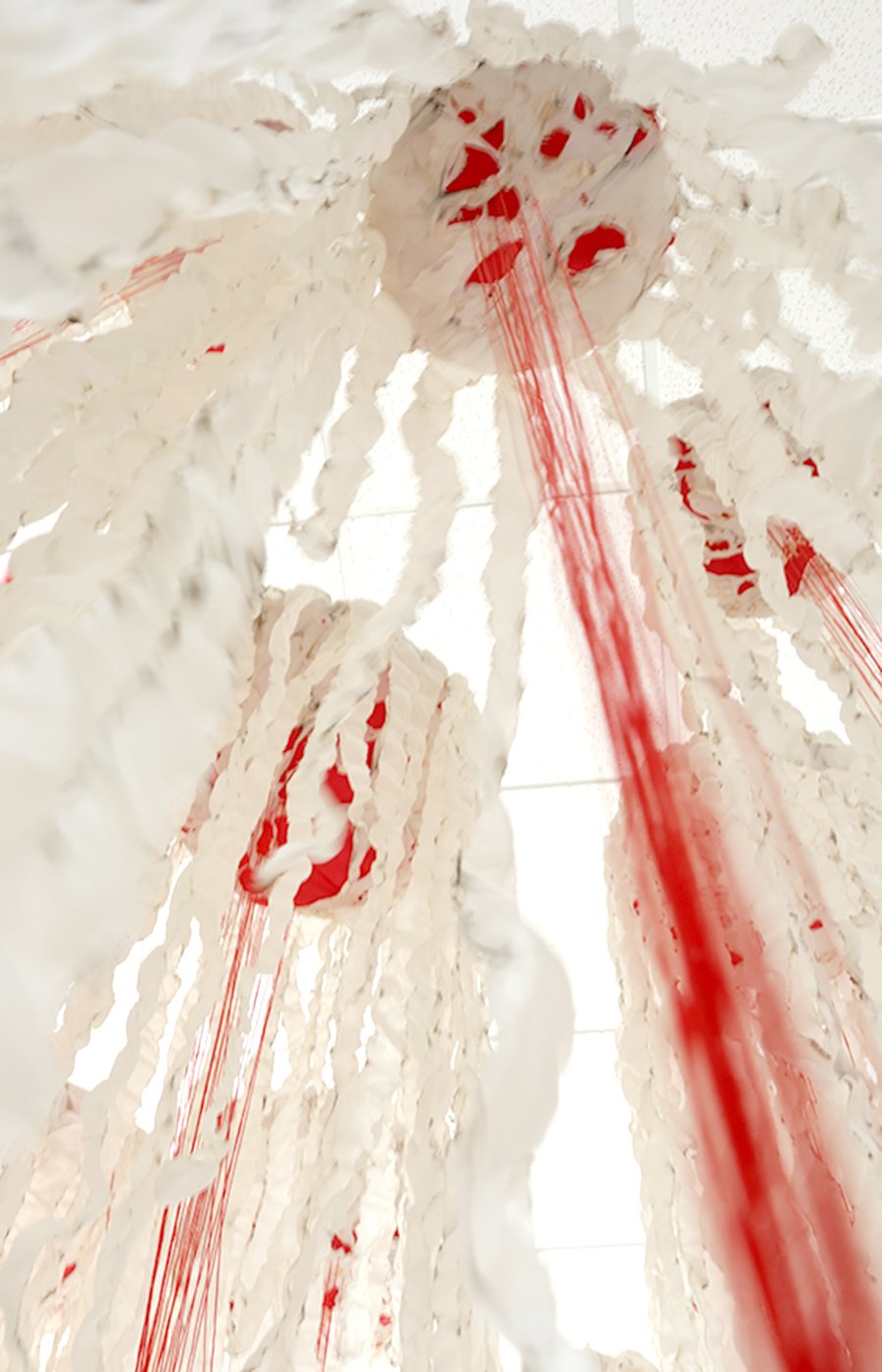 Red threads in textile installation are hanging from above