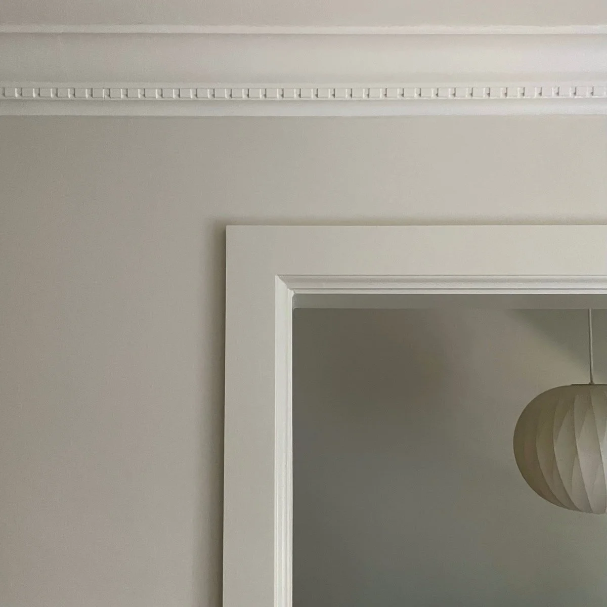 Close-up of a corner of a room showing a white ceiling with decorative crown molding, a white door frame, and a paper light fixture.