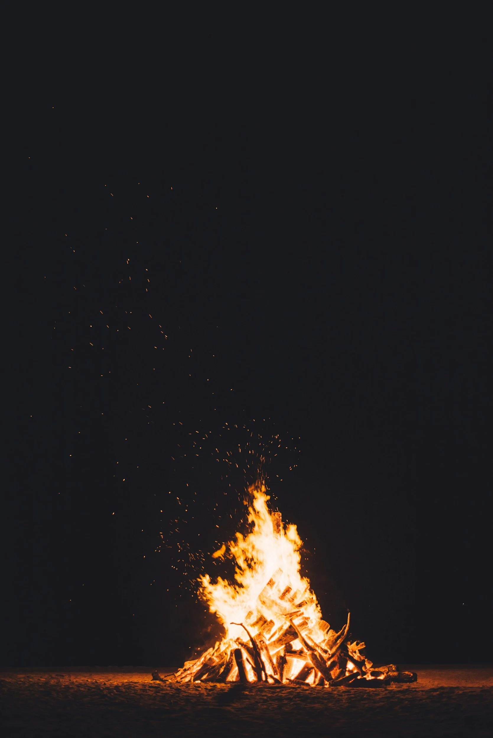 A large bonfire burning on a sandy surface at night with sparks flying upward into the dark sky at a wedding in Tulum