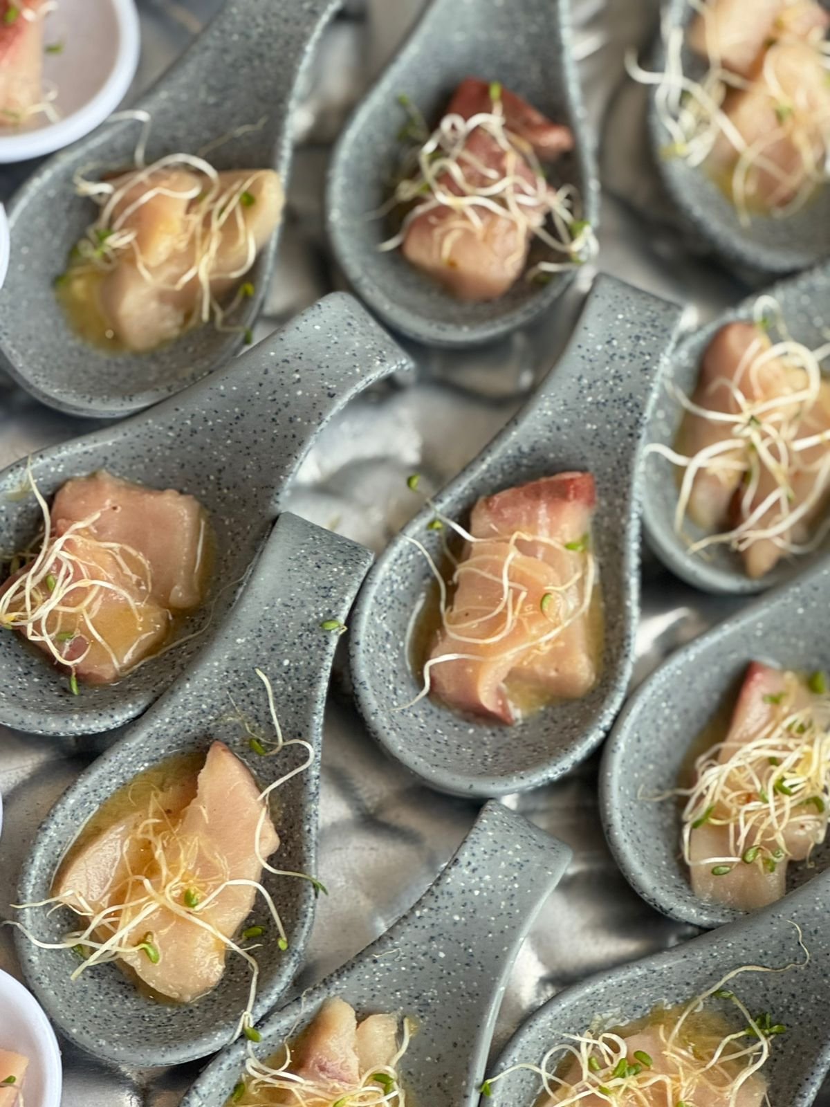 Gourmet tuna tartare appetizers in gray ceramic spoons, topped with sprouts.