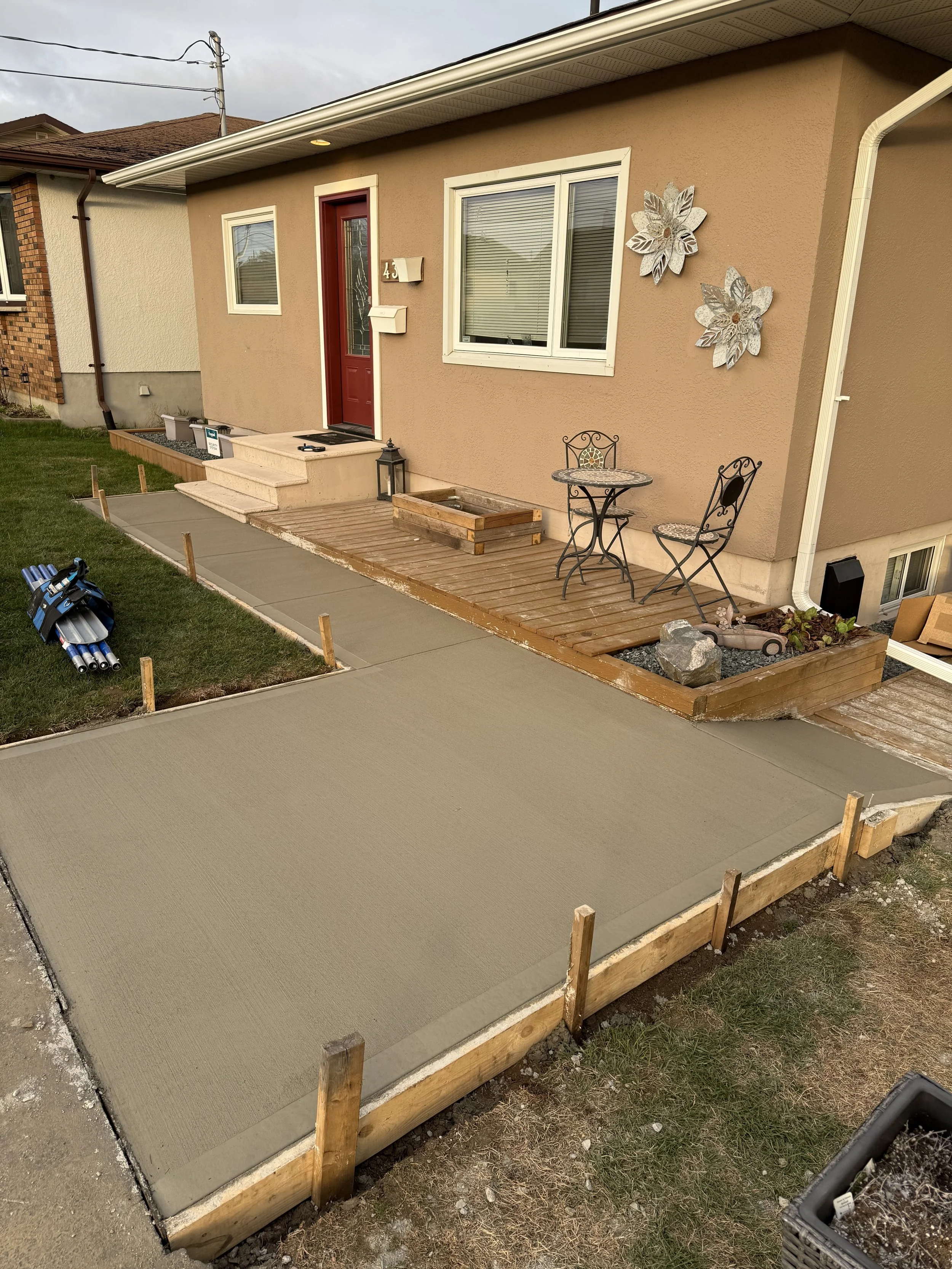 Front porch with concrete slab, wooden deck, and outdoor seating, with a house featuring a red door and decorative wall art, during daytime.