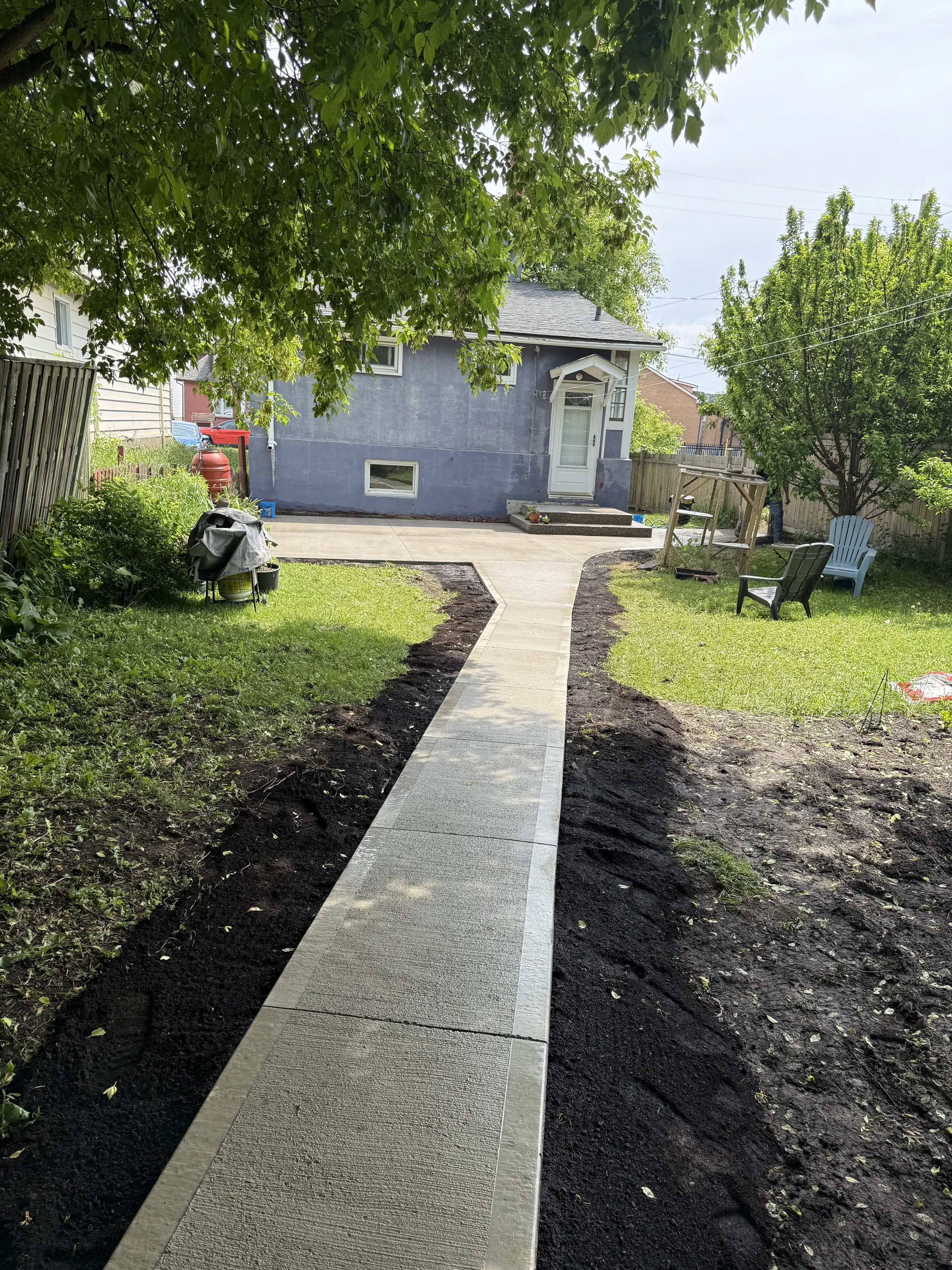 A backyard with a freshly poured concrete broom finished walkway leading to a house.  In Thunder Bay, Ontario