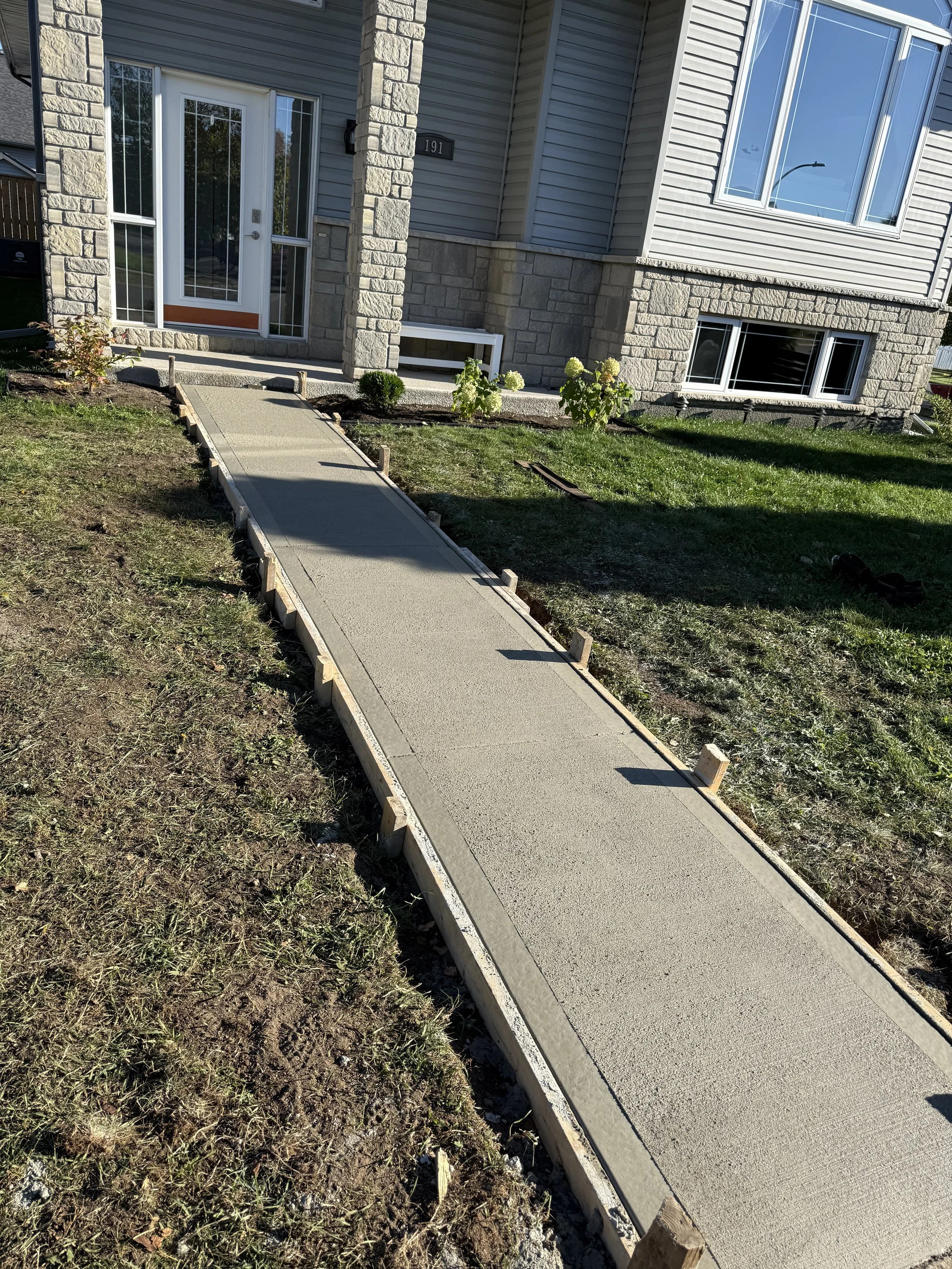 Concrete broom finished sidewalk with control joints under construction leading to front door of house. Thunder Bay, Ontario
