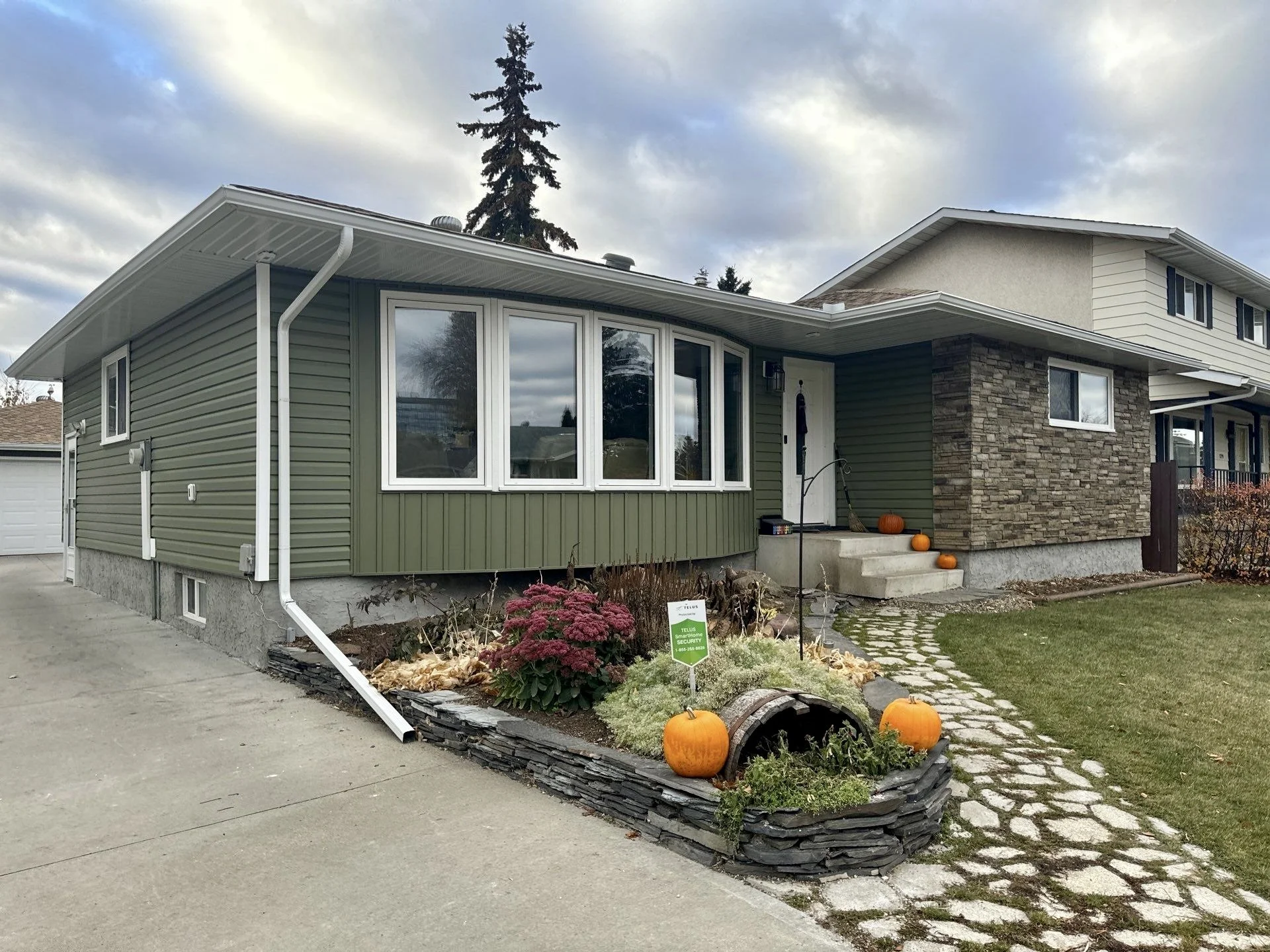 This photo shows a bungalow with new green vinyl siding and a faux masonry accent in Edmonton. Bonus for fall decor!
