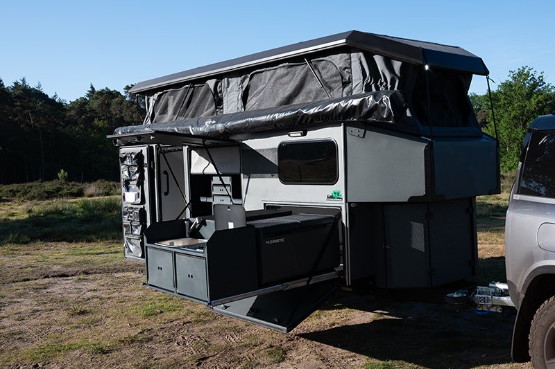 A pop-up BorderX camper trailer set up outdoors in a grassy area, with a vehicle attached to it and a clear sky overhead.