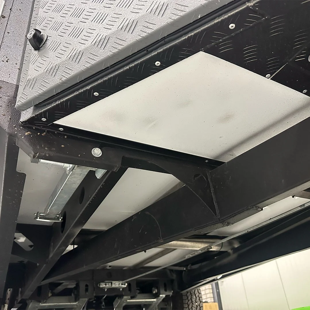 Close-up view of the underside of a vehicle with metal panels, bolts, and structural components visible.