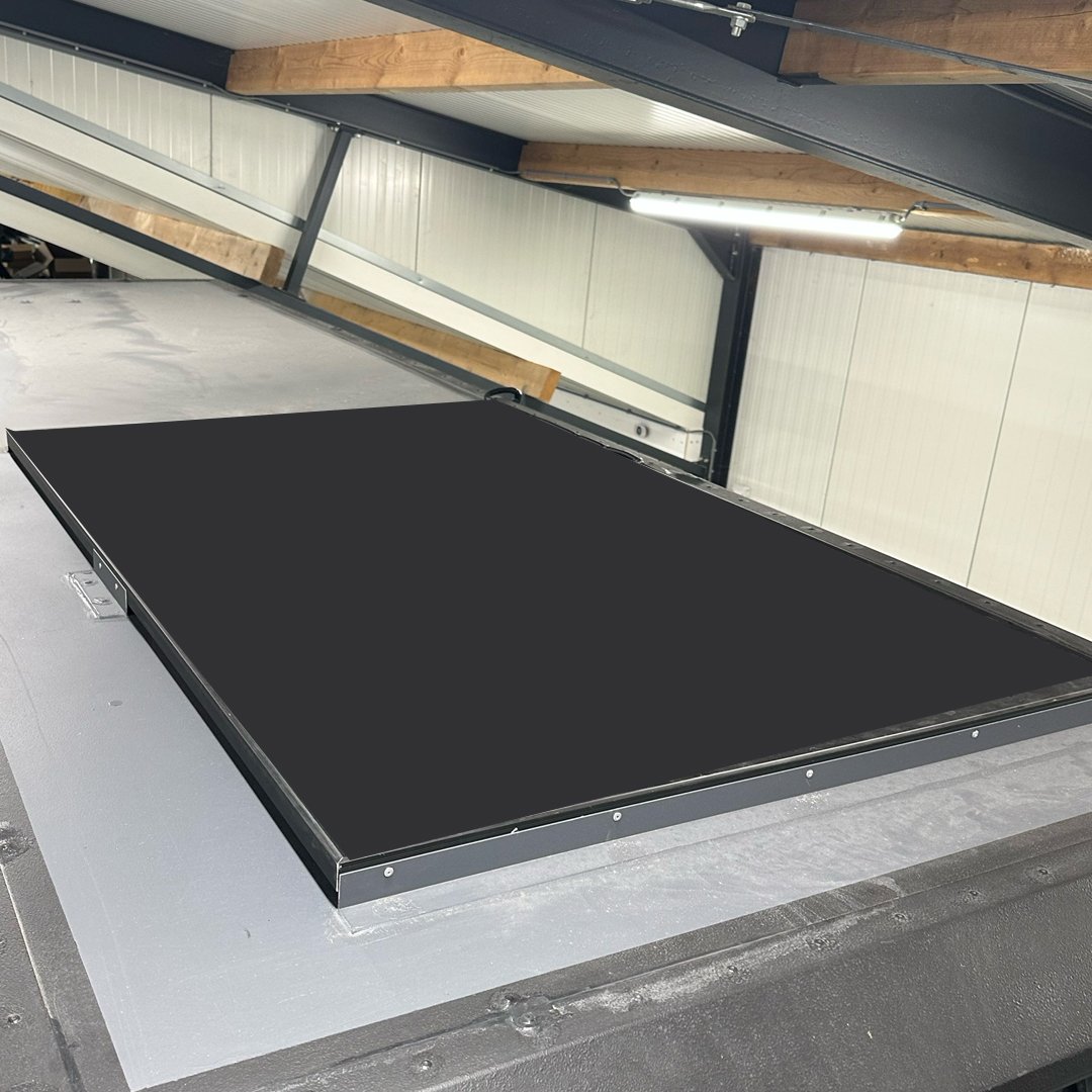Photograph of a large black solar panel installed on a flat rooftop in an industrial or warehouse building.