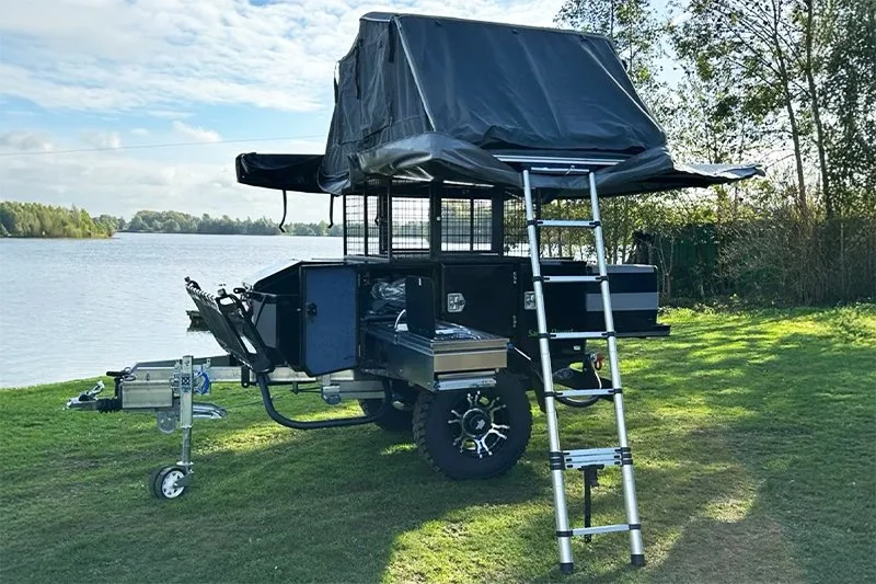 Off-road camping trailer with tent setup by a lake