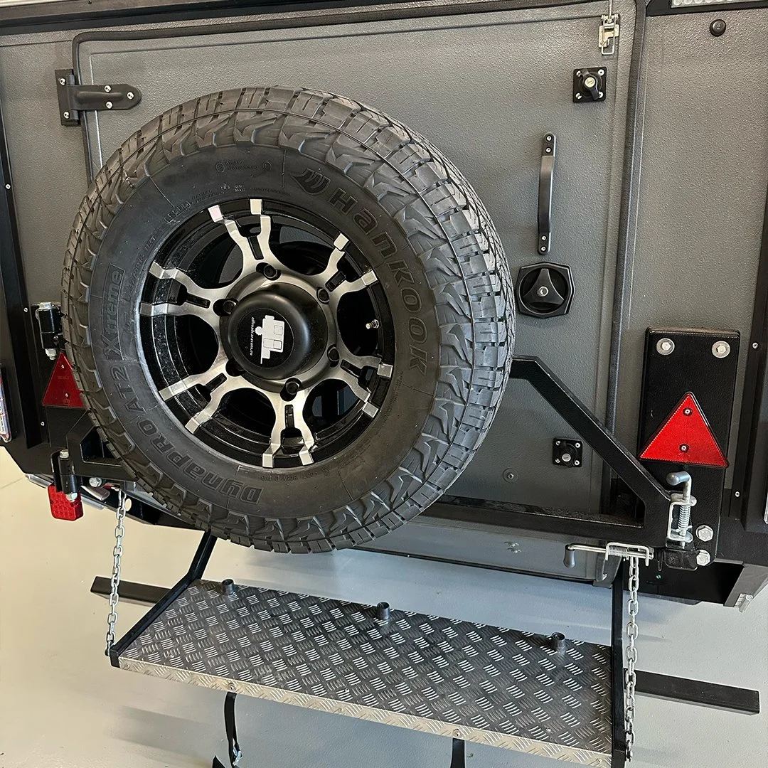 A spare tire mounted on a black rim, attached to a gray metal storage cabinet with various hardware and safety reflectors.