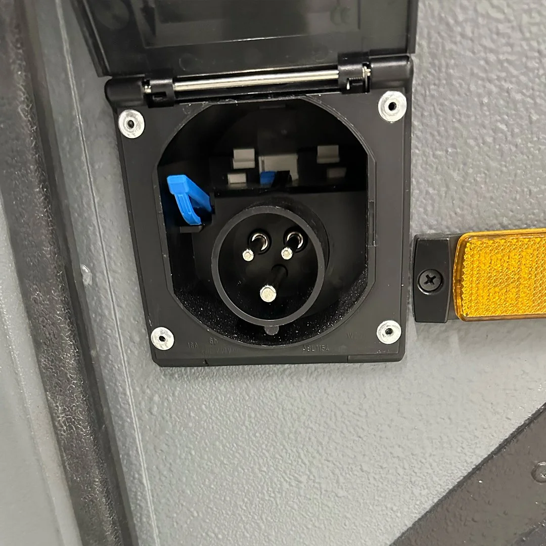 Electrical power outlet on a wall, with an outlet cover open and a blue safety lock inside, and a yellow reflector light to the right.
