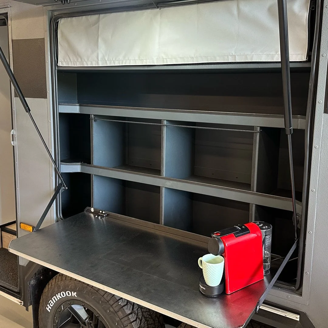 Open storage compartment on a mobile food truck or kiosk with shelves and compartments, with a red coffee machine, a mug, and a water bottle on the extended countertop.