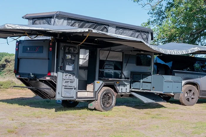 A gray BorderX cargo trailer with an extendable pop-up roof set up in an outdoor area, connected to a gray pickup truck.