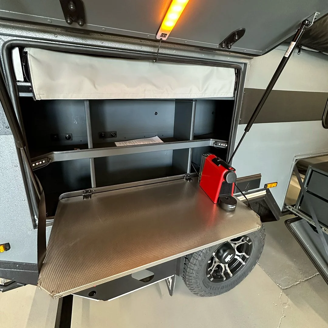 Open storage compartment on a mobile trailer with a fold-down workspace, a red portable generator, and a small black-and-silver portable device.