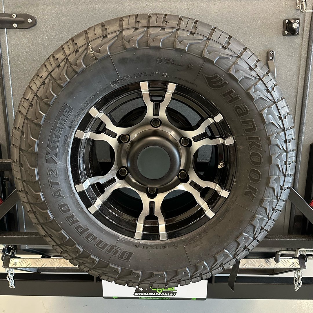 A close-up of a black off-road tire with a black rim, mounted on a display stand in a garage or workshop setting.
