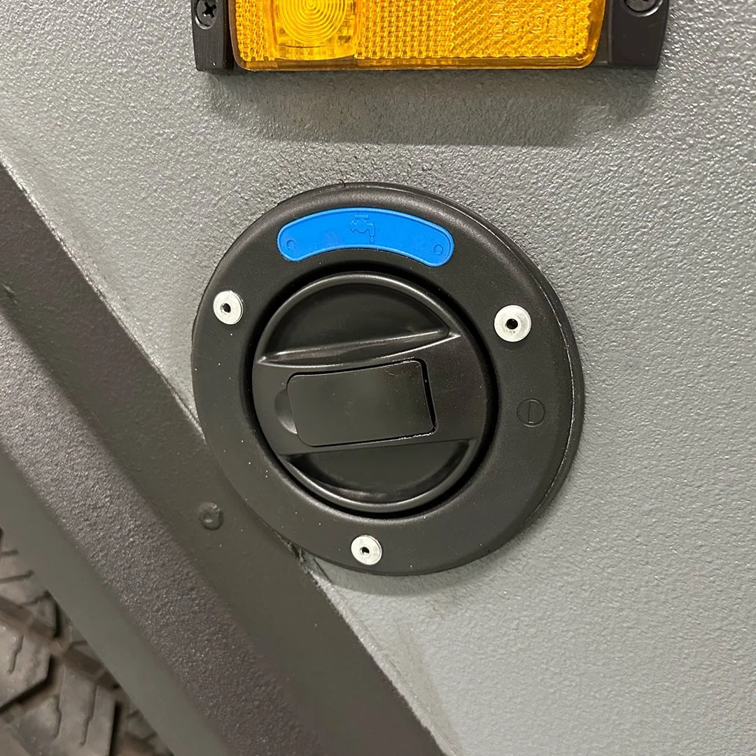 Close-up of a black circular power outlet with a blue water faucet symbol on it, mounted on a textured gray surface.