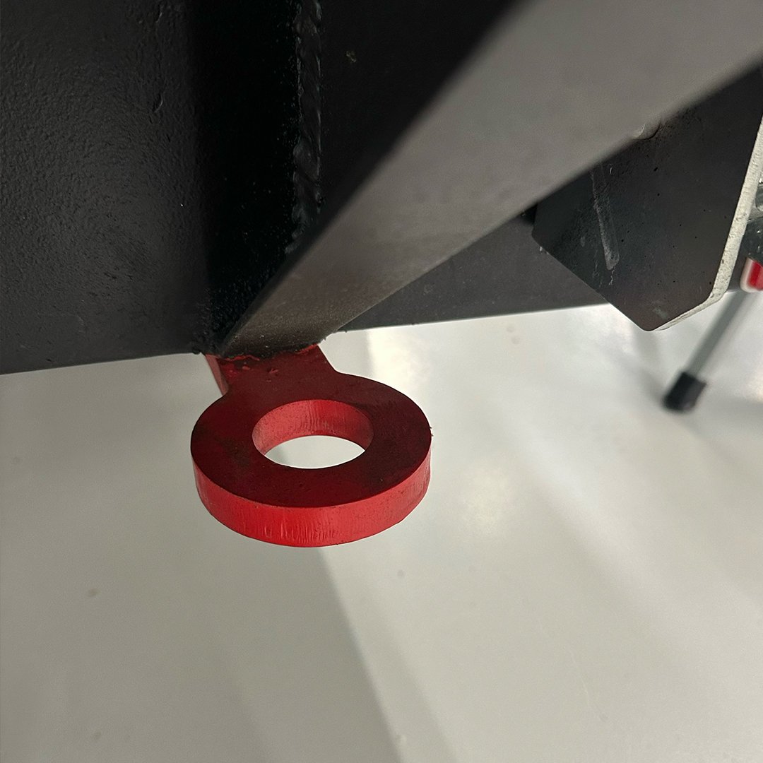 Close-up of a red, circular lifting eye attached beneath a black metal structure, possibly part of industrial equipment or machinery.