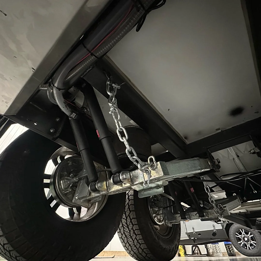Underside view of a vehicle showing tires, suspension, and secured chains.