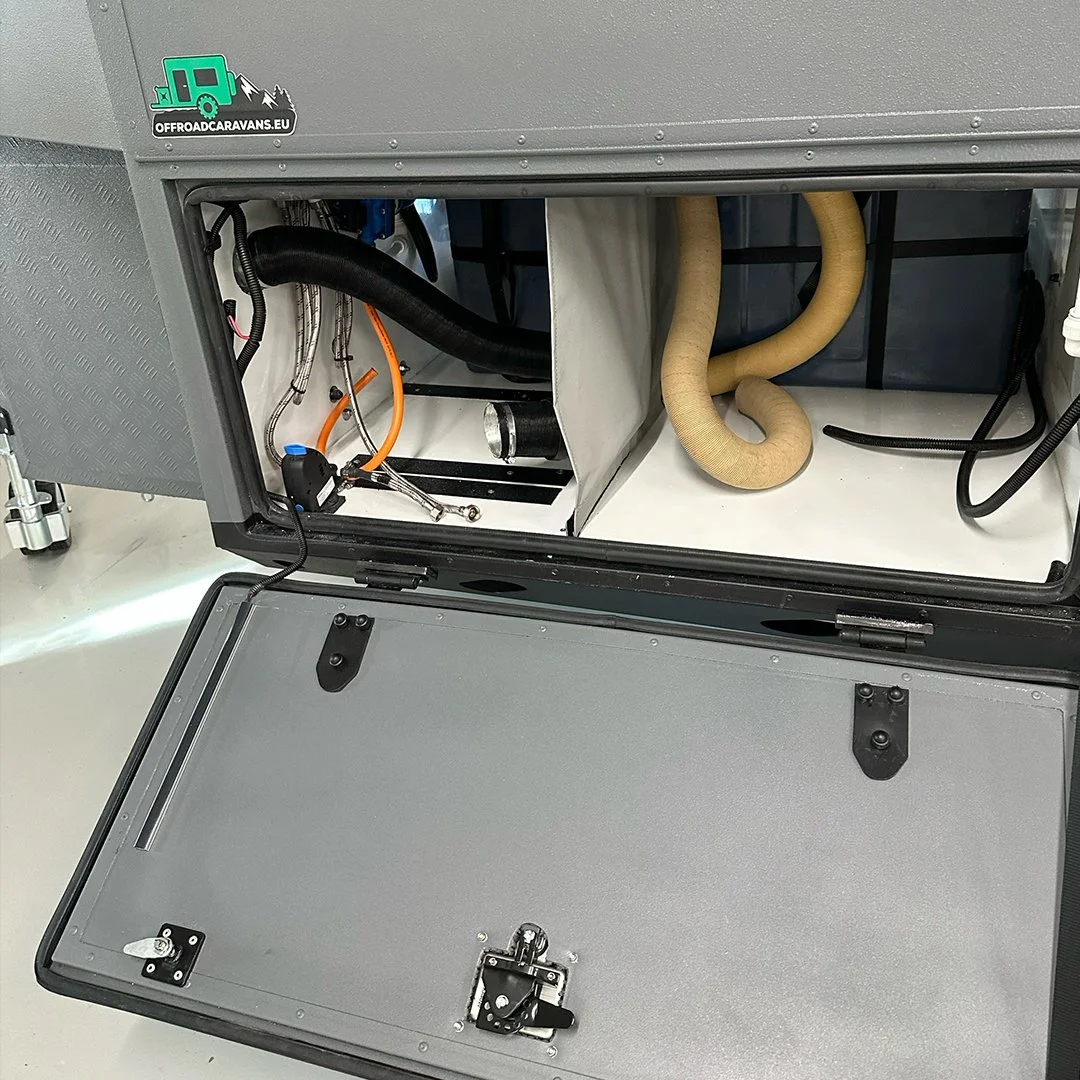 Open compartment of a gray off-road vehicle showing hoses, wires, and mechanical parts inside.