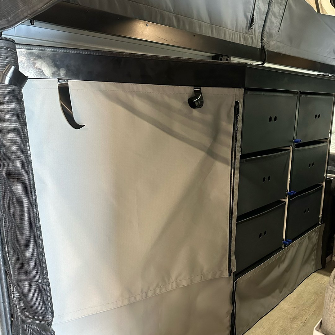 A storage unit with black drawers and a beige cover, partially open, situated next to a black mesh bag.