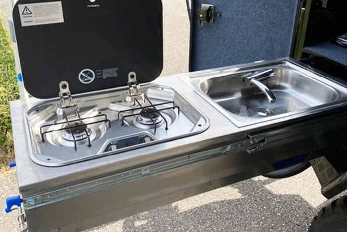 Compact outdoor kitchen setup with two-burner stove and sink.