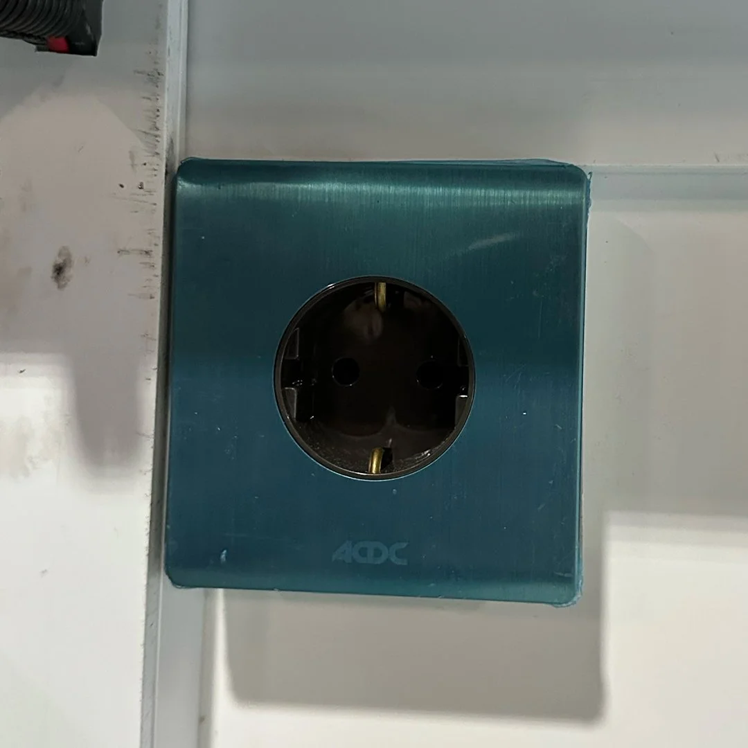 Electrical outlet on a wall with a blue plastic cover and visible grounding prongs.