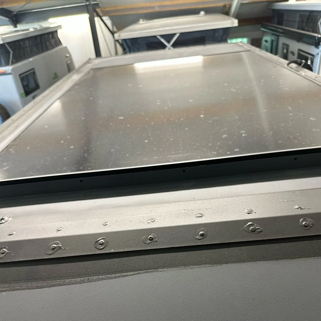 A close-up of a metal roof with water droplets on it, part of a larger machine or vehicle surrounded by other equipment in a storage or workshop area.