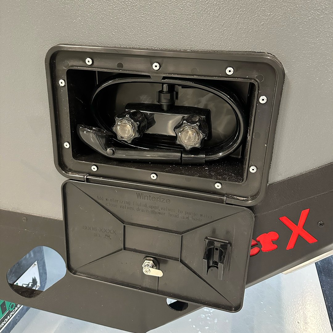 A commercial ice maker with the front panel open, showing the water inlet valve and the ice mold inside.