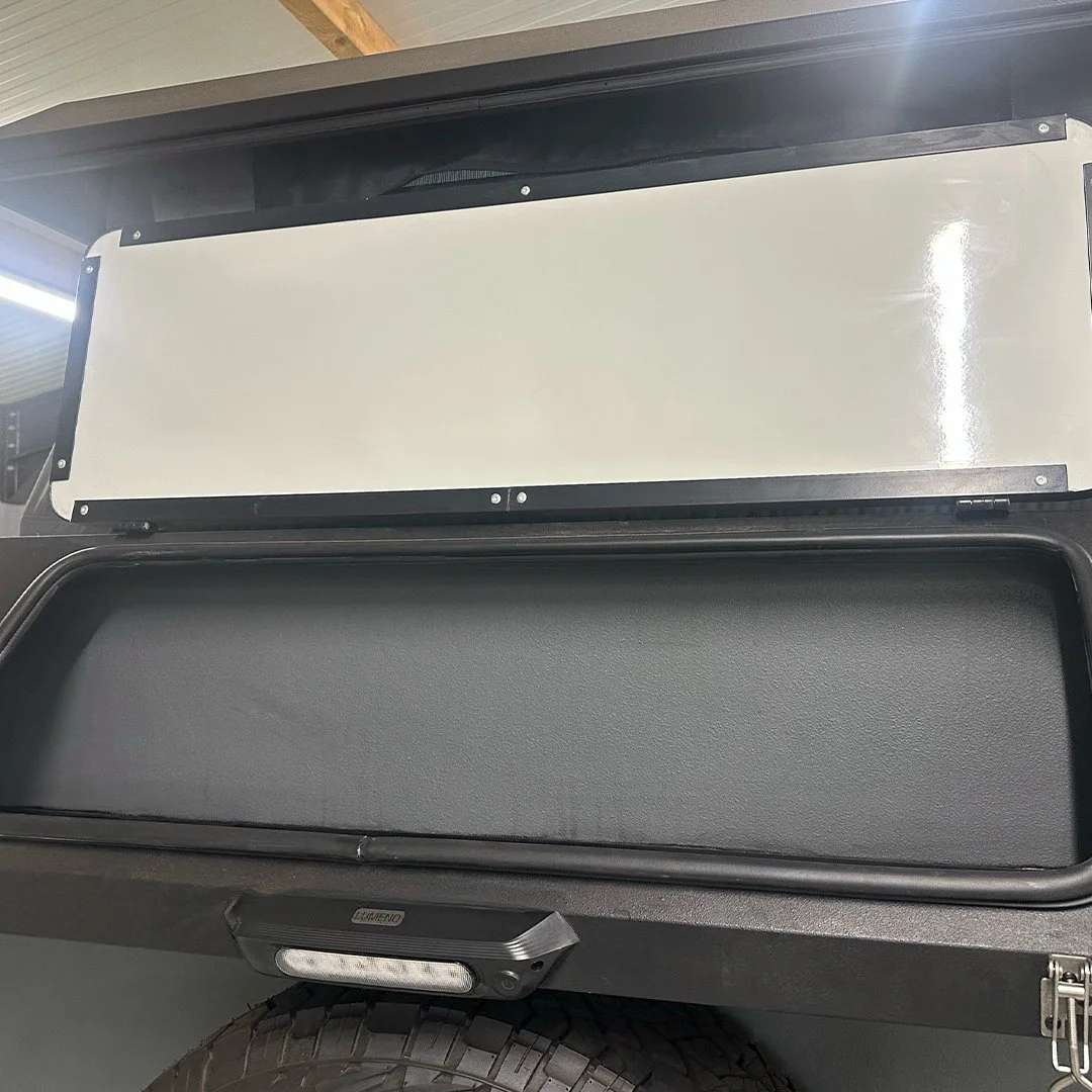 Close-up of the side of a black utility vehicle, showing a large white empty storage compartment with lid, and a small light on the front of the compartment.