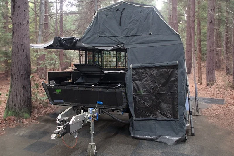 Camper trailer with extended tent setup in a forested area