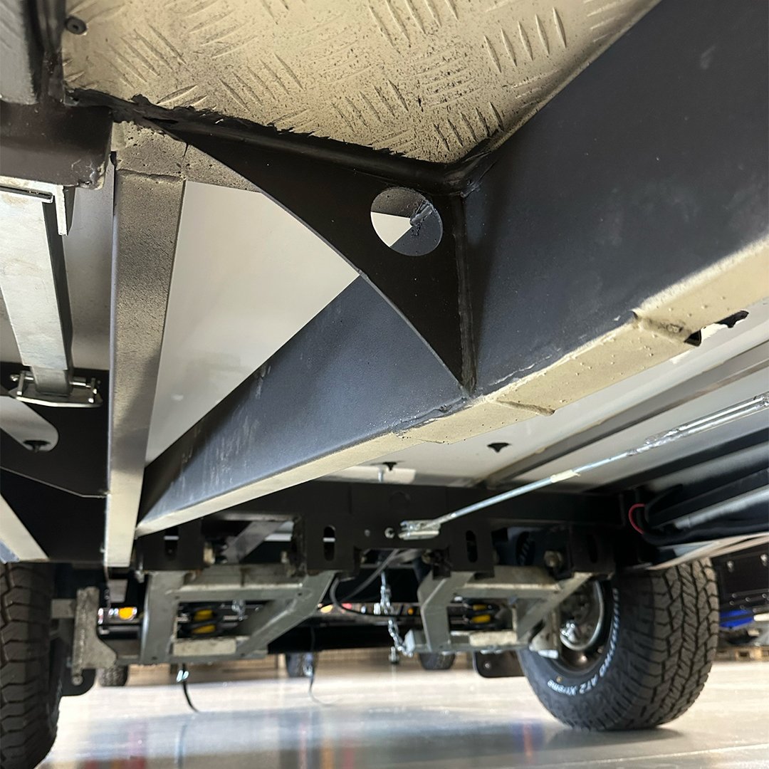 Underneath view of a vehicle showing metal framework, suspension components, tire, and part of the chassis.