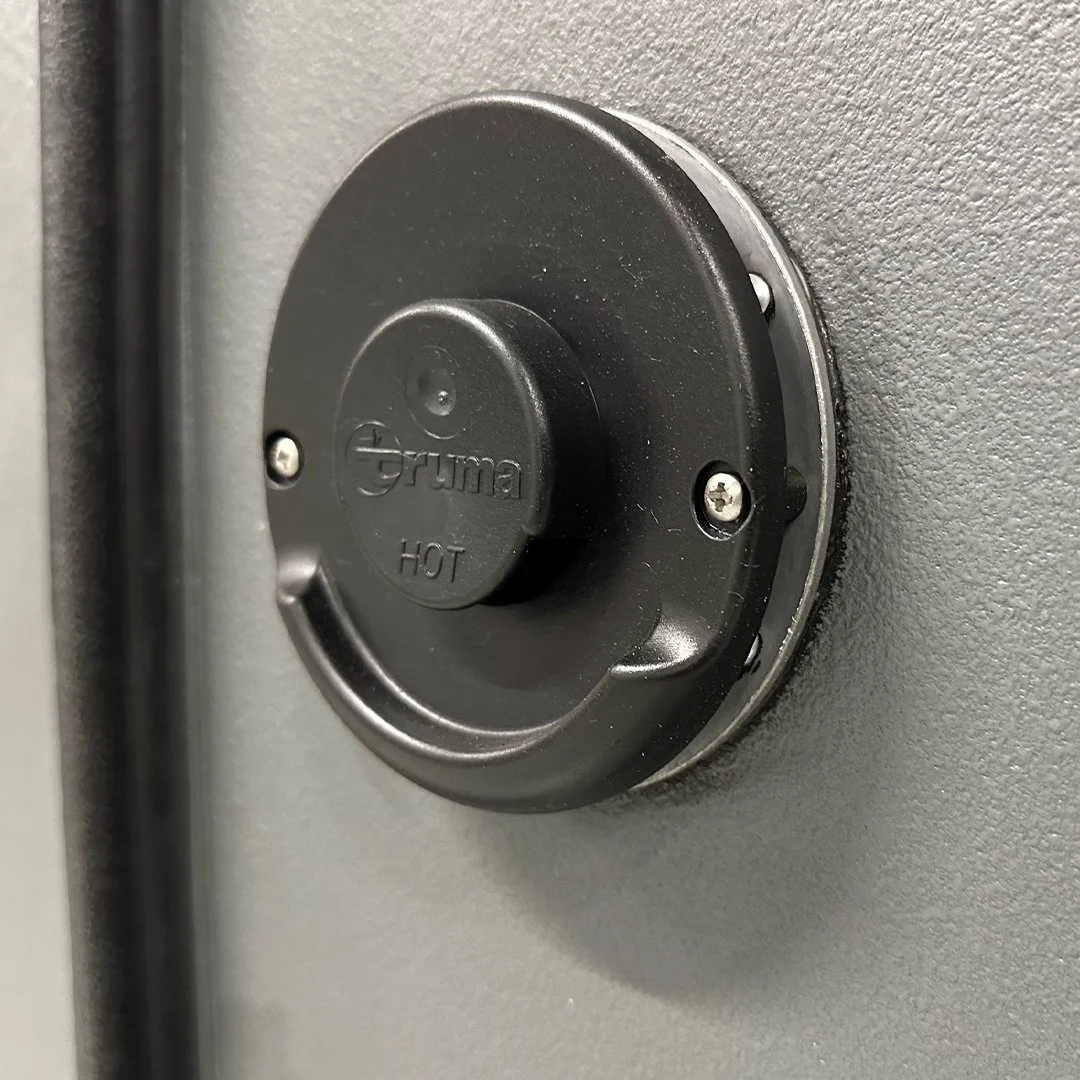 Close-up of a round black control knob labeled "gruma" with "HOT" written underneath, mounted on a gray surface.