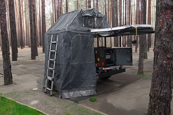 Off-road camper trailer with rooftop tent and ladder in a forest setting.
