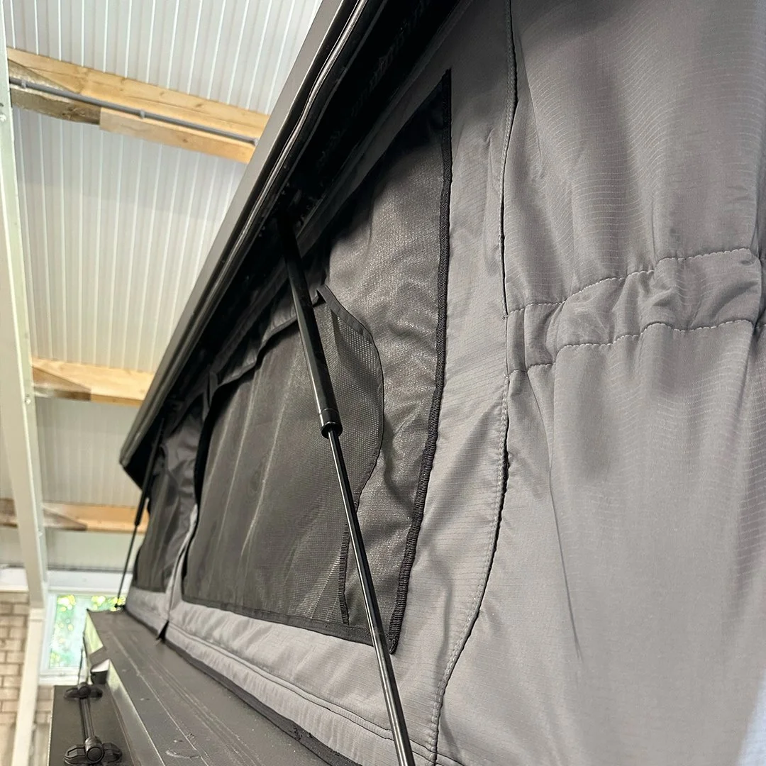 Close-up of a black and gray truck bed cover with support rods, installed on a pickup truck inside a garage.
