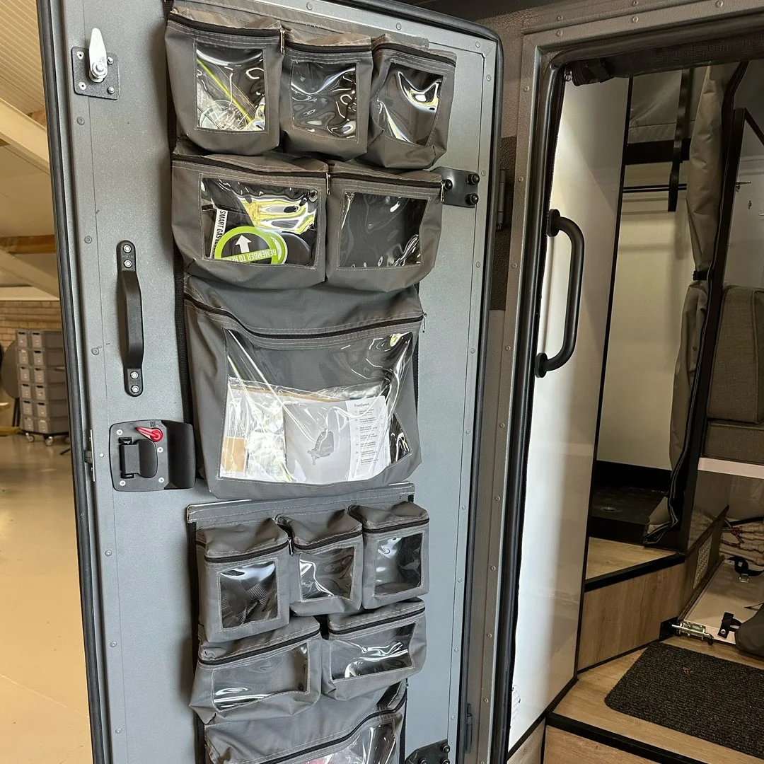 An interior view of a vehicle with gray fabric organizer pockets mounted on the door, containing various items including a first aid kit, a maintenance tool, and manuals.