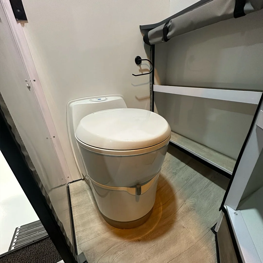A modern white toilet with a lid, placed in a small bathroom space next to a cabinet with a gray curtain or cover.