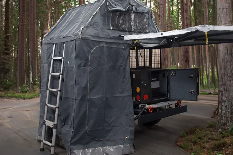 Mobile camping unit with rooftop tent and awning in forest setting.