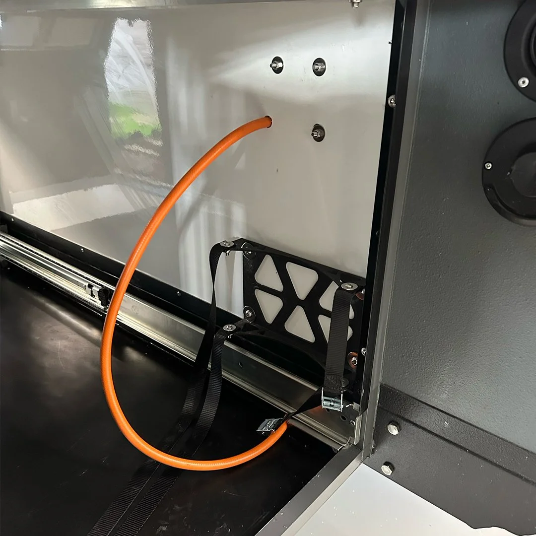 Close-up of the inside of a metal enclosure with an orange cable connected, and a black strap securing a small metallic component.