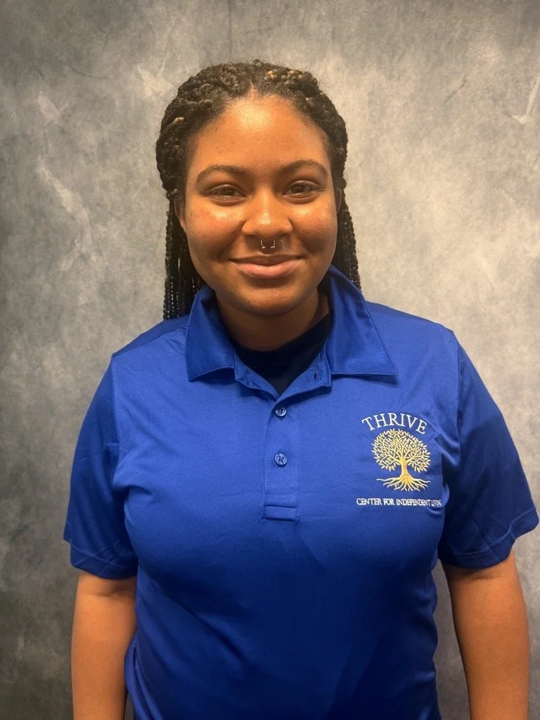 A black woman with long black hair wearing a blue polo with Thrive Center for Independent Living on it.
