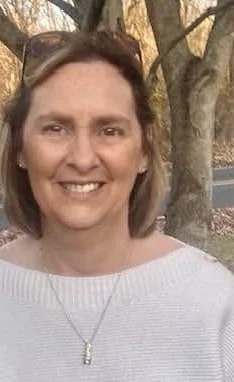 The image contains a blonde white woman in front of a tree.