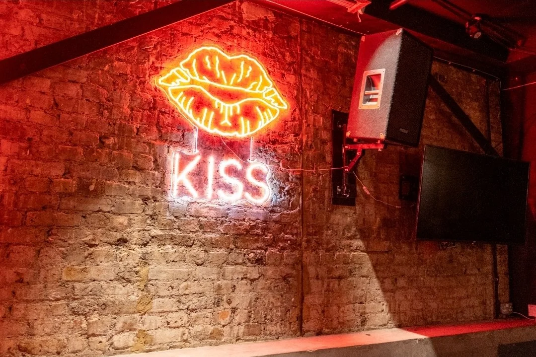 Neon sign of red and yellow lips with the word "KISS" in pink neon on a brick wall