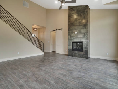 Spacious living room with wooden floors, high ceiling, modern fireplace, and staircase with black railing.