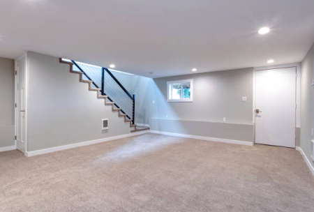 Empty finished basement room with carpet, staircase, and small window.