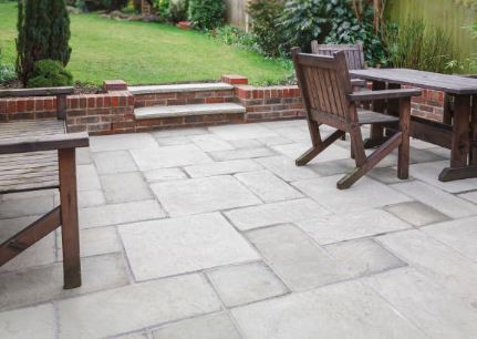 Stone patio with wooden furniture next to a garden with steps leading up to a grassy area.